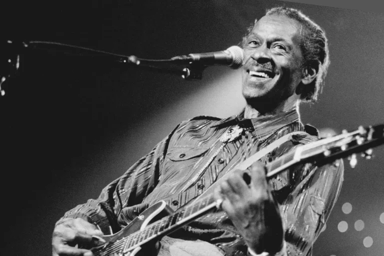 Chuck Berry smiling guitarist singing into a microphone while playing on stage, conveying joy, confidence, and lasting influence in live rock music.