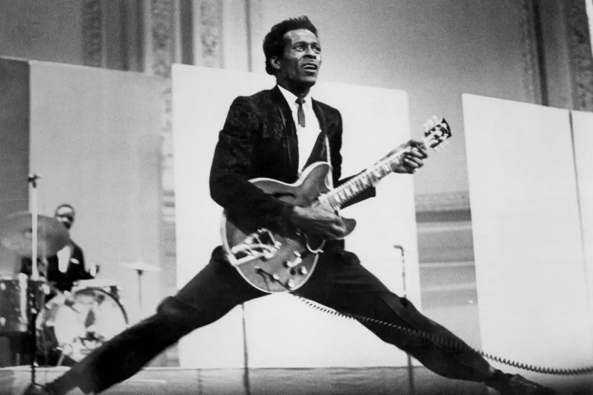 Chuck Berry mid-jump on stage while playing an electric guitar, capturing the energy and showmanship that defined early rock and roll performances.