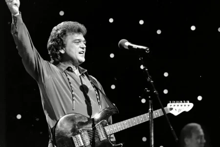 Conway Twitty raising his arm while playing electric guitar on stage, captured in a dynamic black-and-white performance moment.