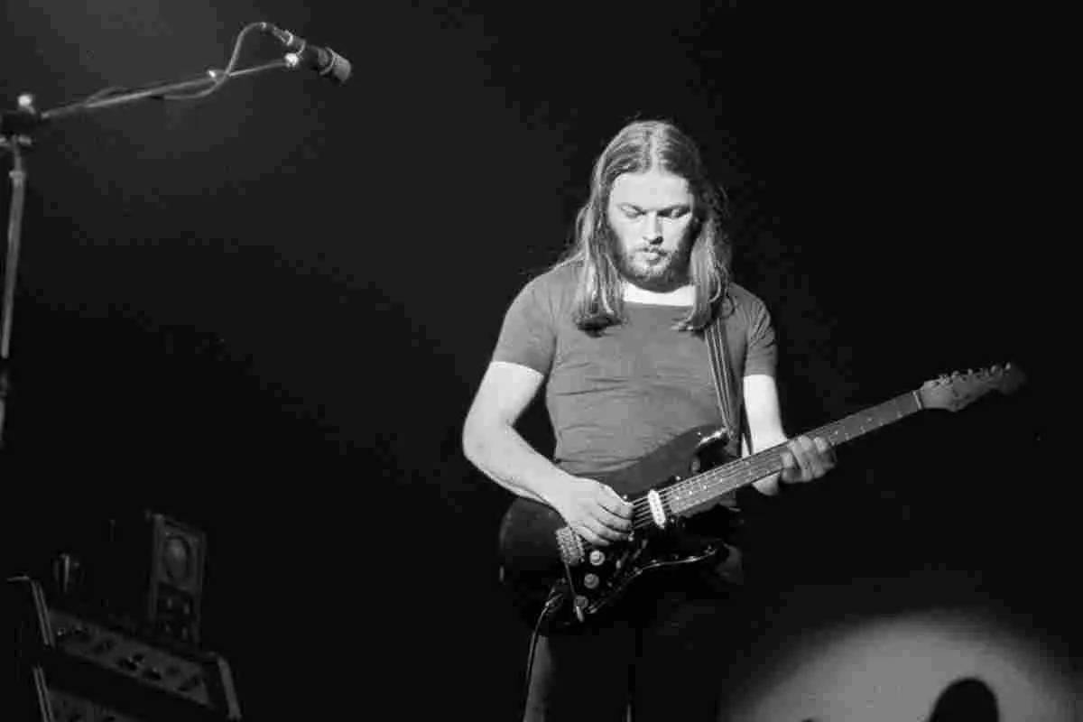 David Gilmour performing live in a black-and-white photo, focused on his guitar.