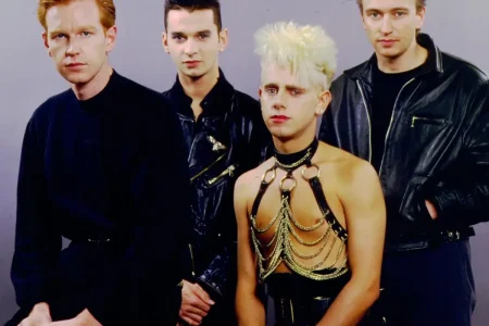 Depeche Mode with one wearing a striking harness-style outfit, posed against a plain background.