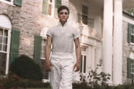 Elvis Presley walking confidently toward the camera wearing a light gray short-sleeve shirt.