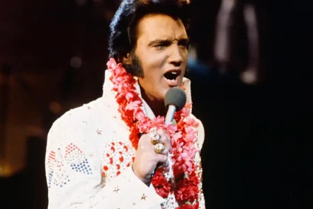 Elvis Presley singing into a microphone while wearing a white.