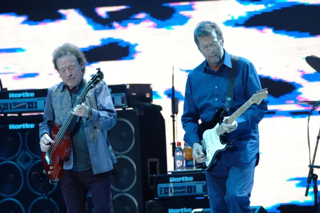Eric Clapton and Jack Bruce: The Brilliant, Volatile Partnership That Shaped Rock Eric Clapton and Jack Bruce play electric guitars side by side during a large live concert, with amplifiers and a bright stage backdrop behind them.