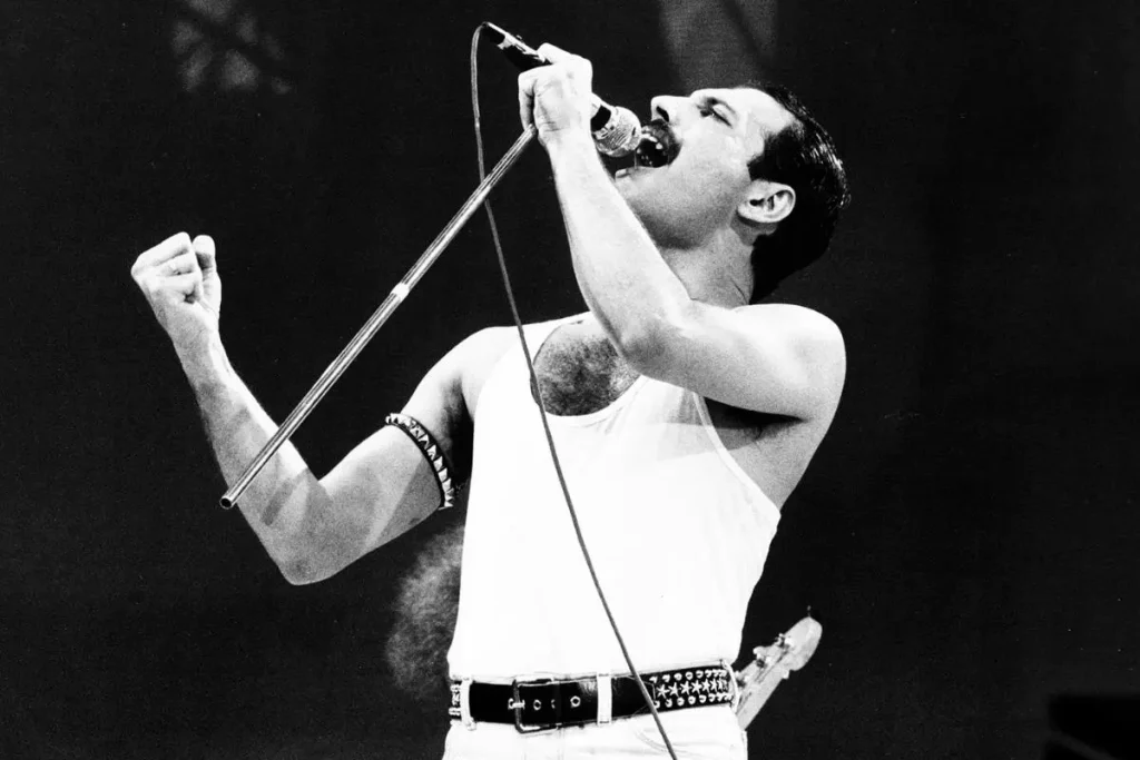 Queen’s “I Want It All”: The 1989 Power Anthem Freddie Never Sang Live Freddie Mercury passionately into a microphone with one fist raised, captured mid-performance in a dramatic black-and-white concert photograph.