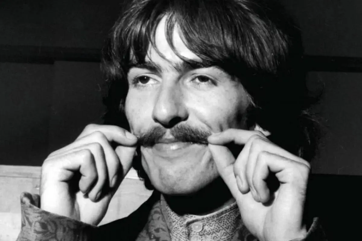 George Harrison playfully holding his mustache.