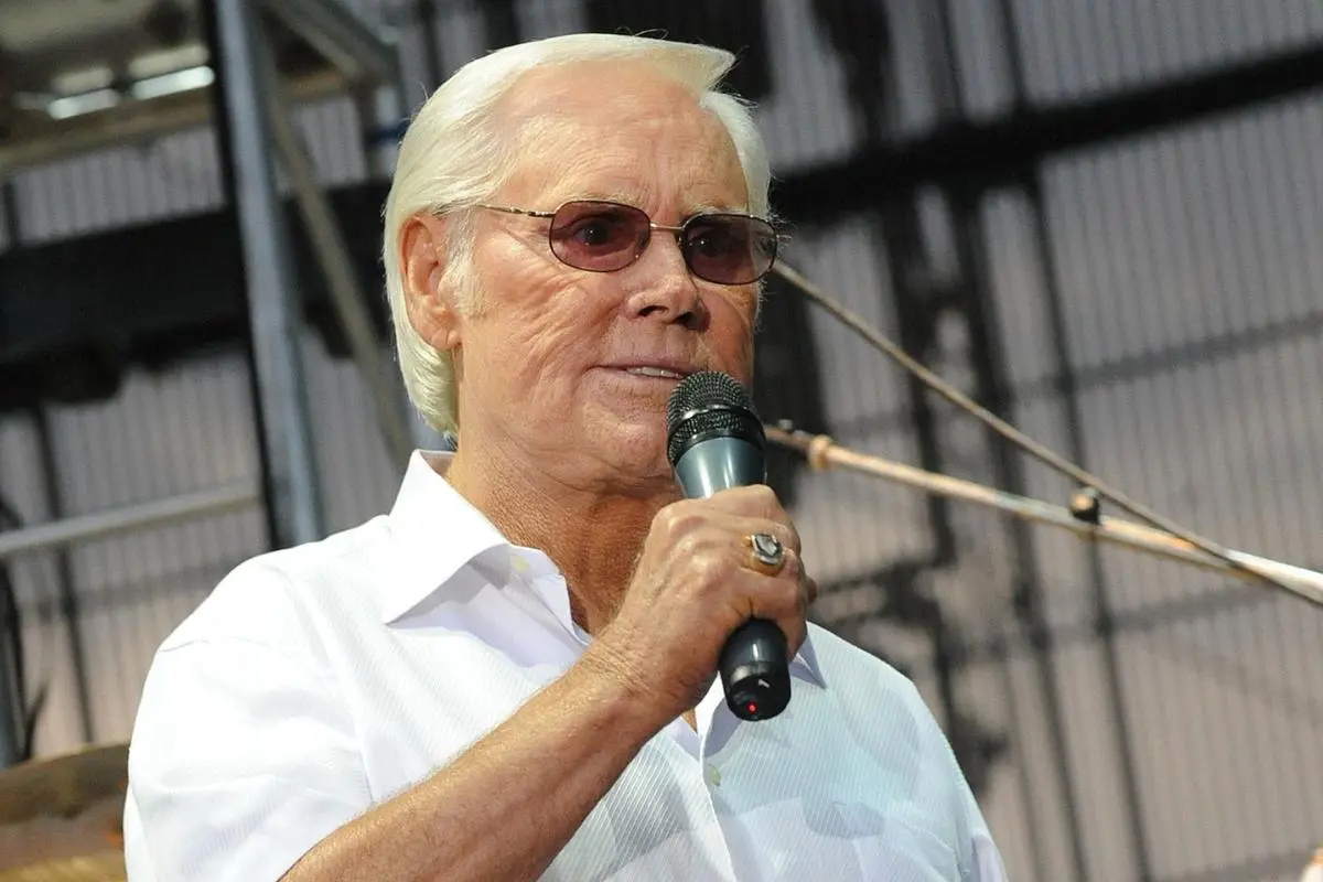 George Jones stands on stage wearing a white shirt and tinted glasses.