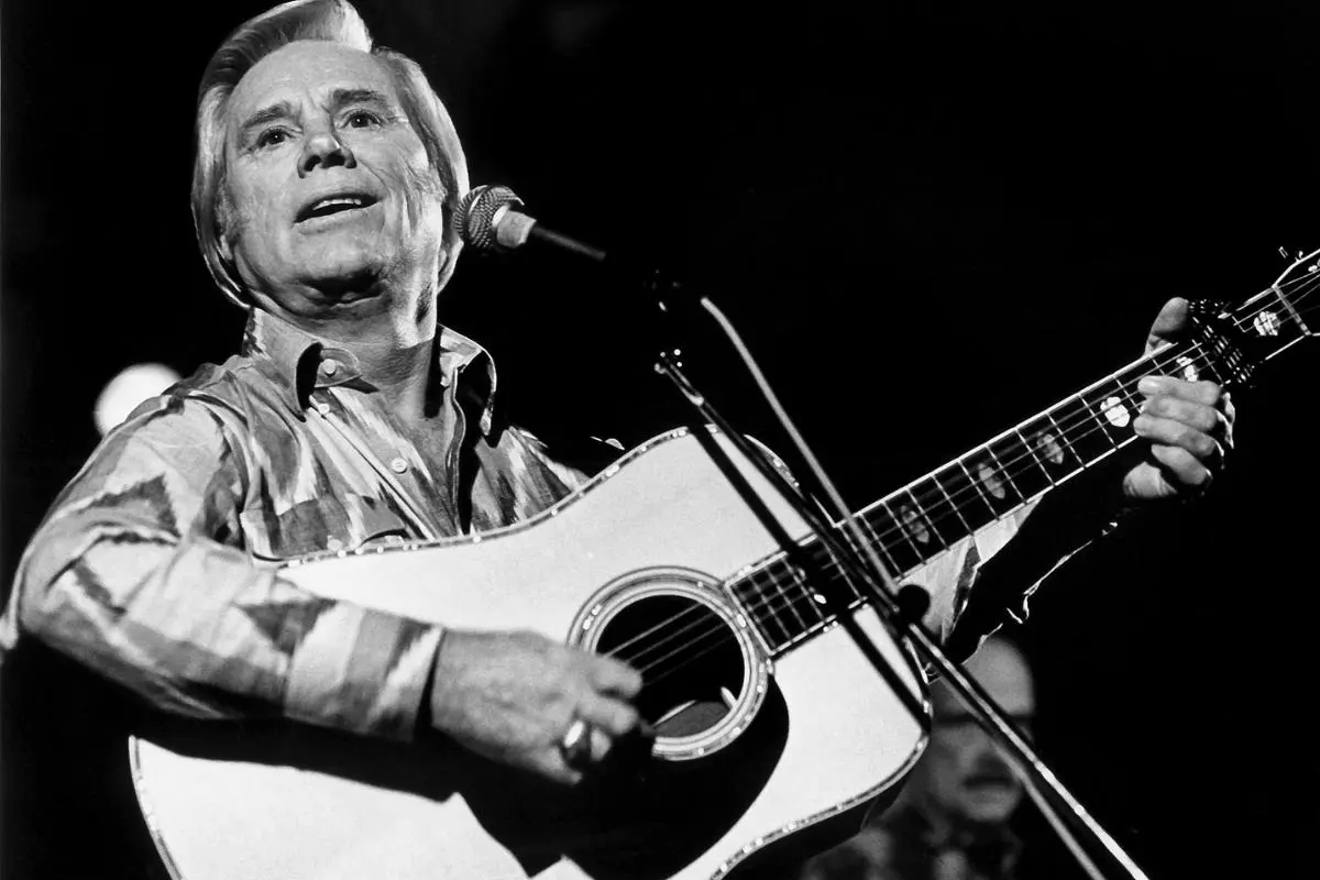 George Jones singing and playing an acoustic guitar on stage, looking upward toward the audience.