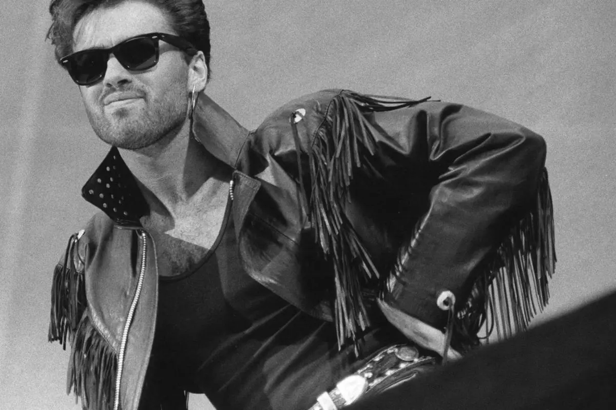 George Michael leaning forward confidently against a bright outdoor background.