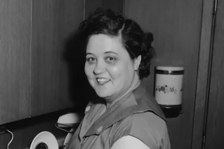 Gladys Love Presley smiling in a kitchen, wearing a sleeveless dress with curled hair.