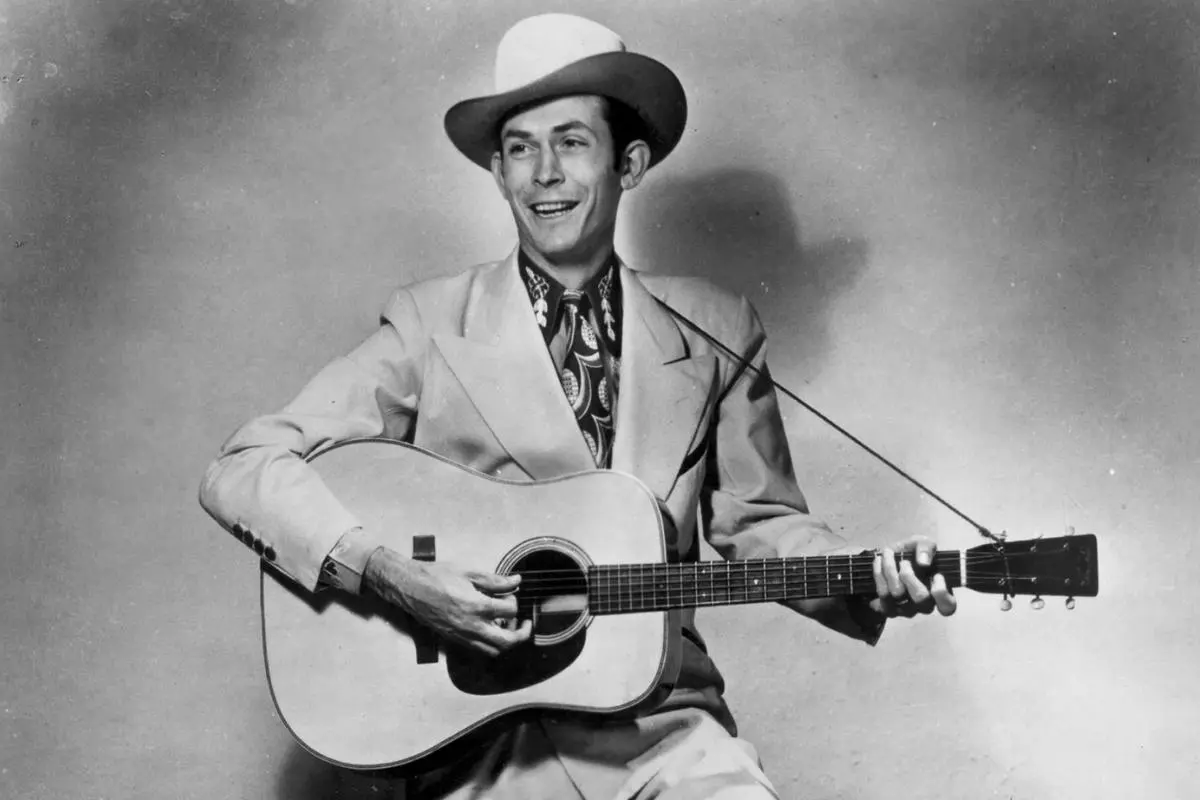 Hank Williams holding an acoustic guitar and smiling while performing.