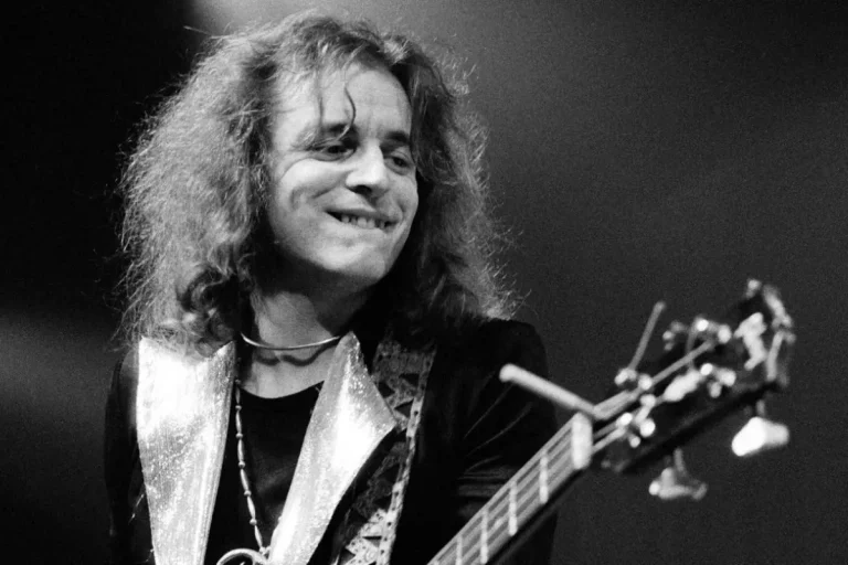 Jack Bruce smiling while playing on stage, conveying joy, confidence, and musical connection during a live performance.
