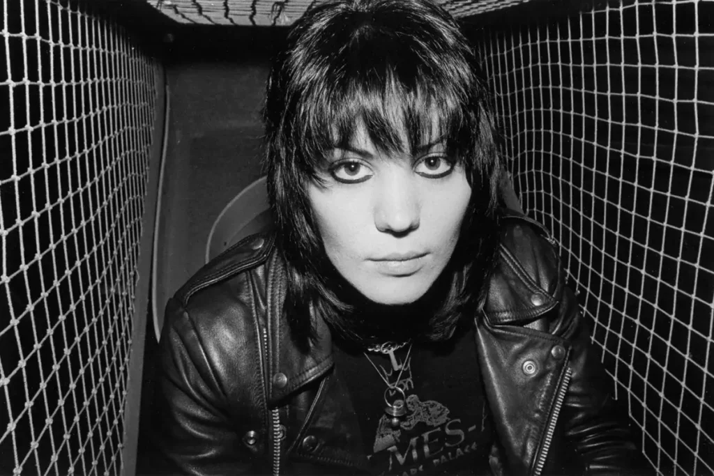 Joan Jett wearing a leather jacket, staring directly into the camera from a narrow enclosed space, conveying intensity, defiance, and punk-era attitude.
