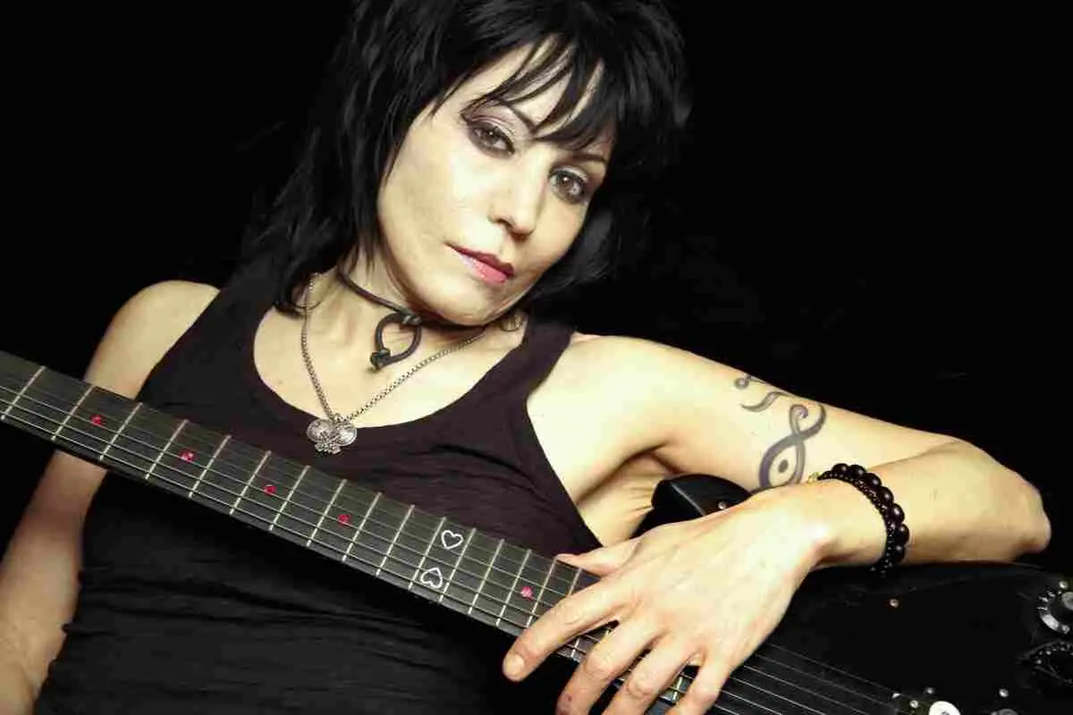 Joan Jett posing with electric guitar against a dark background