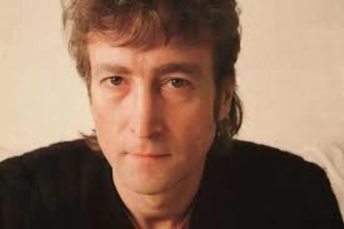 John Lennon with short brown hair, looking directly at the camera with a calm, neutral expression.