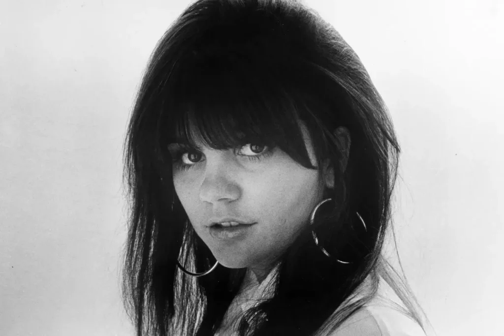 Linda Ronstadt in a black-and-white close-up, wearing hoop earrings and looking over her shoulder, emphasizing her iconic 1970s rock image.