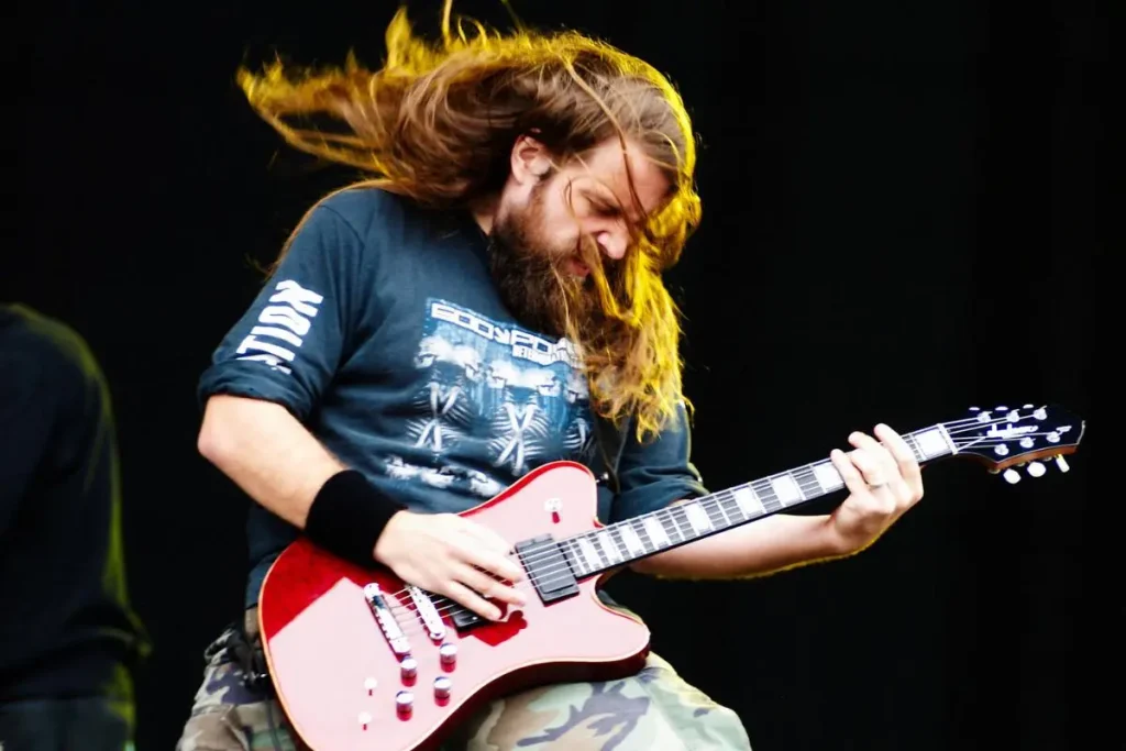 Mark Morton performing live on stage, long hair flying as he plays a red electric guitar.