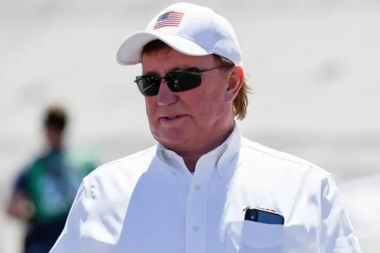 Marty Robbins wearing a white baseball cap, dark sunglasses, and a white button-down shirt, standing in bright sunlight with a phone visible in his shirt pocket.
