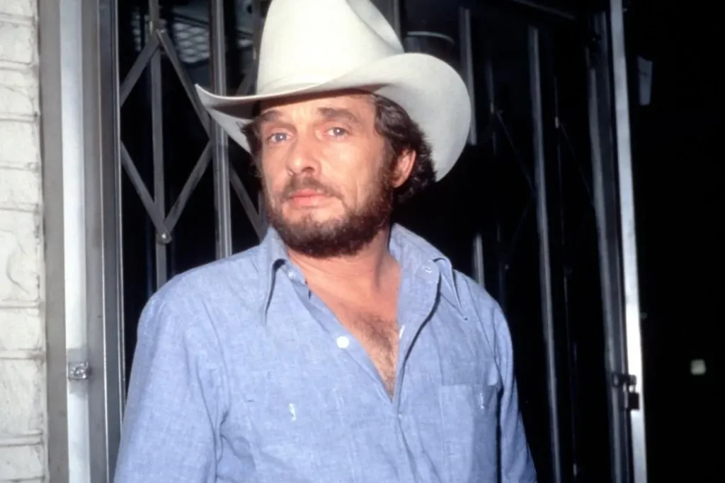 Merle Haggard’s “Sing Me Back Home”: The San Quentin Memory That Became a Country Prayer Merle Haggard wearing a white cowboy hat and light blue button-down shirt.