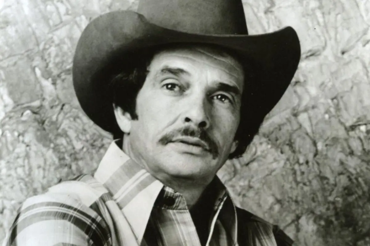 Merle Haggard in a cowboy hat and plaid shirt, with a mustache.