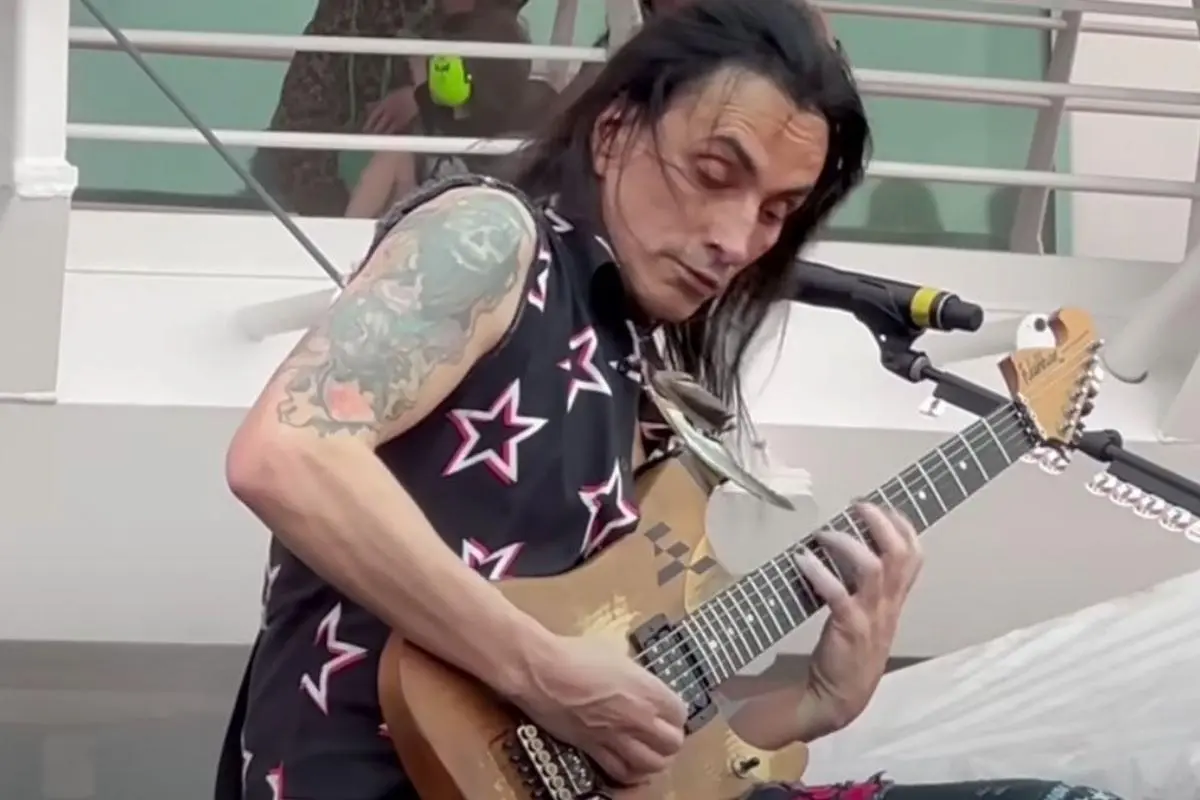 Nuno Bettencourt performs an intricate solo on an electric guitar, standing near a microphone with an intense, focused expression during a live performance.