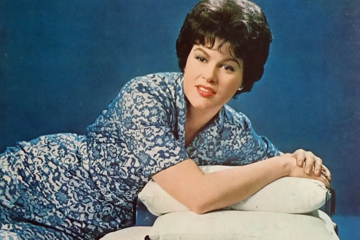 Color studio portrait of Patsy Cline reclining in a patterned dress, conveying classic mid-century glamour associated with her iconic music era.