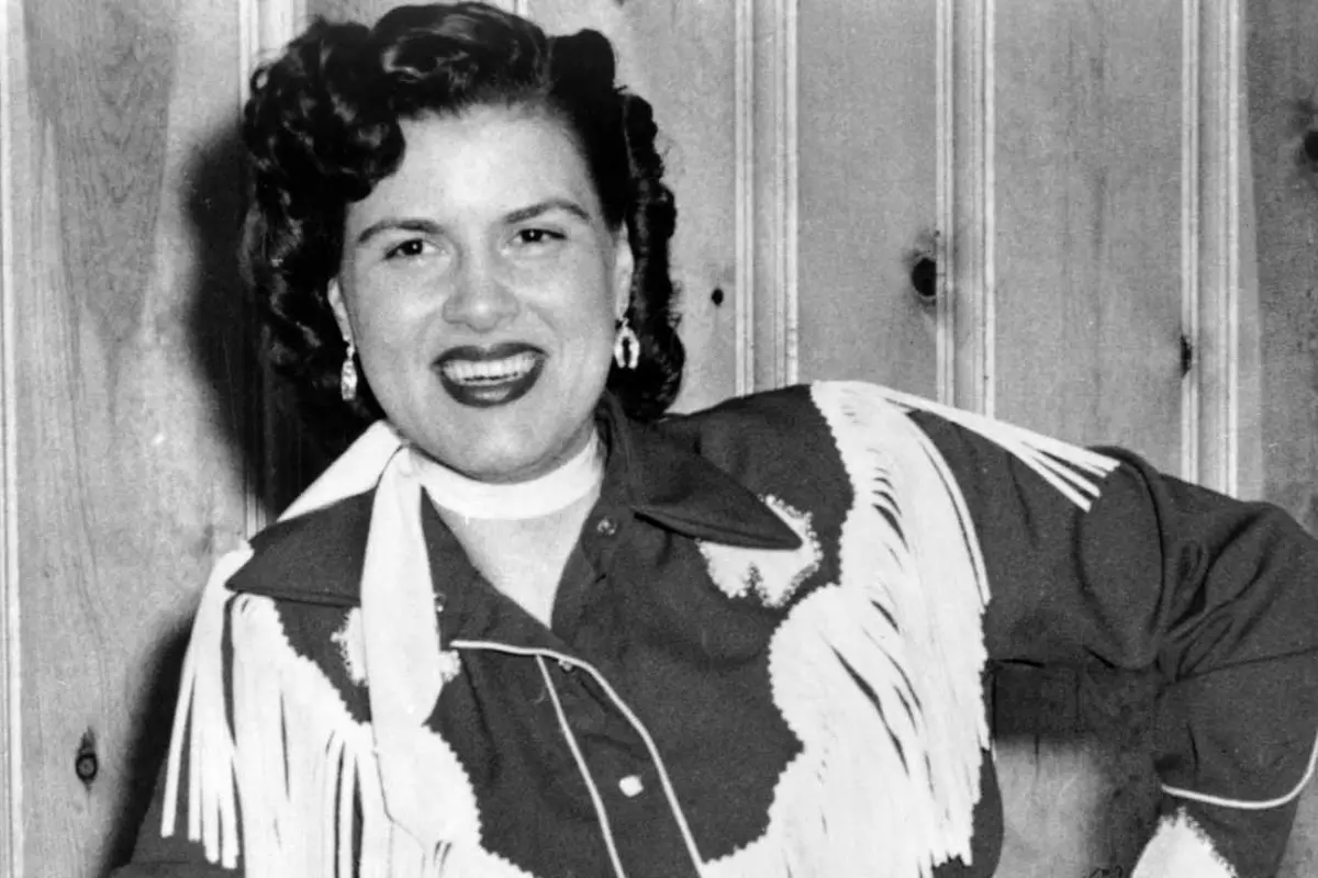 Black-and-white photo of Patsy Cline wearing a fringed Western-style outfit, highlighting her roots in traditional country music and performance style.