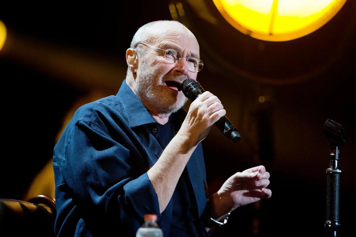 Phil Collins performs during a live concert, singing into a microphone with expressive gestures.