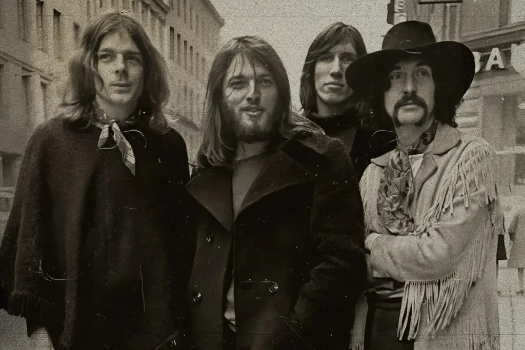 Pink Floyd in their early years, standing together on a city street wearing coats and scarves, looking directly at the camera.