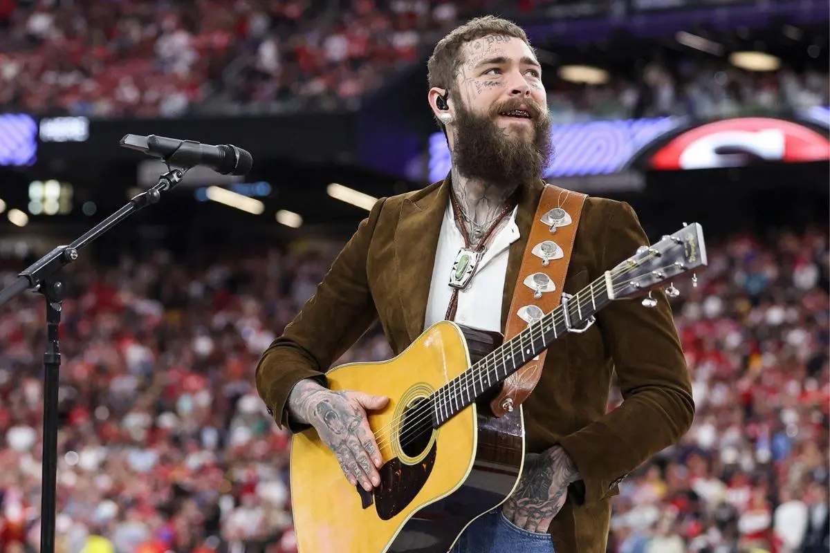 Post Malone performs with an acoustic guitar in a packed stadium.