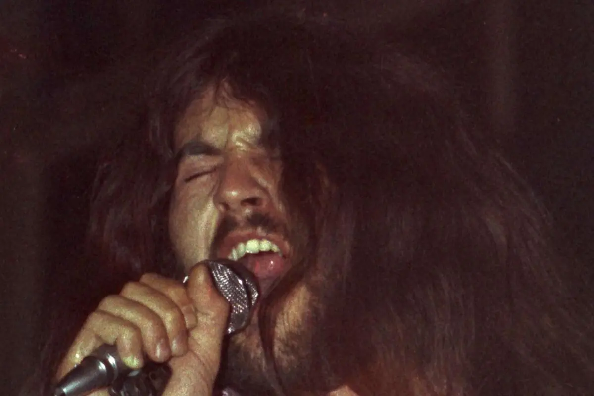 Ritchie Blackmore singing intensely into a microphone on stage with long hair during a concert.