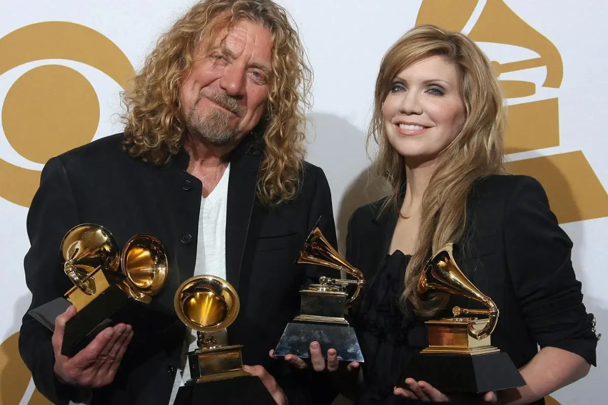Robert Plant pose on a red carpet holding multiple gold gramophone awards.