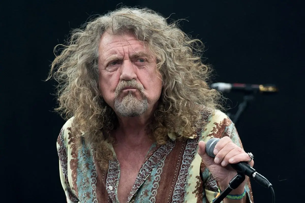 Robert Plant performs on stage, gripping a microphone with an intense expression under concert lighting.