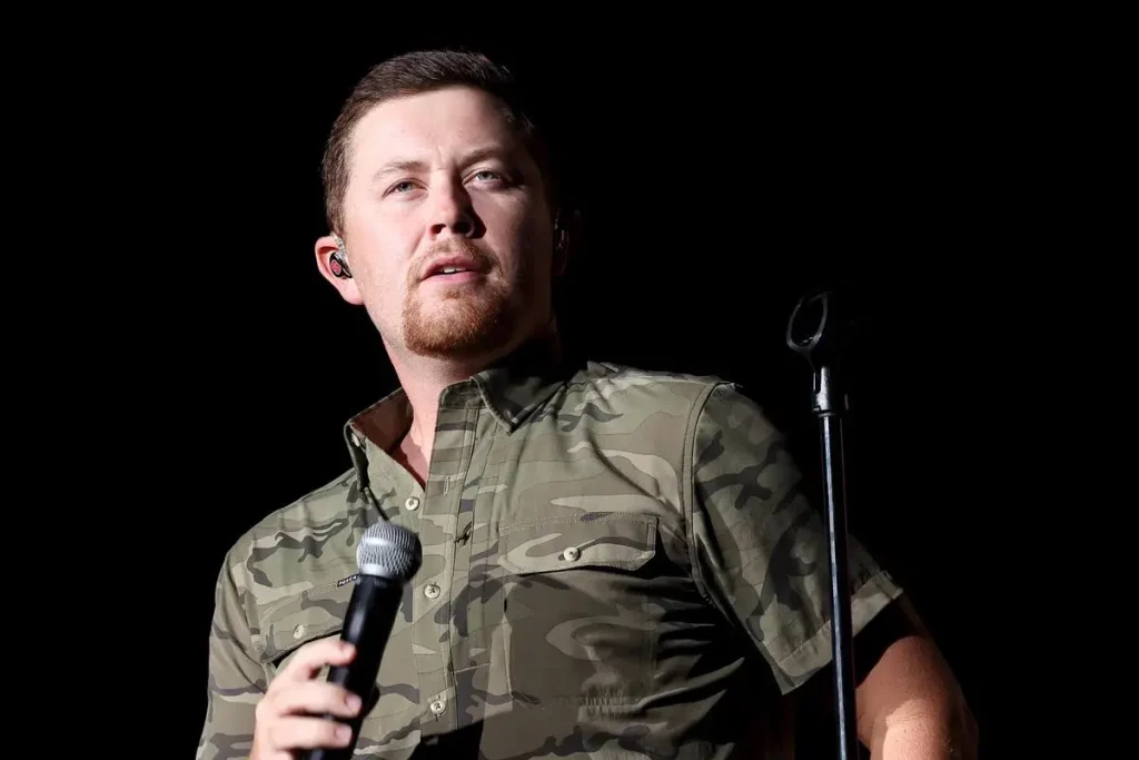 Scotty McCreery Sings “Hello Darlin’” at the Opry: A Conway Twitty Tribute Done Right Scotty McCreery holding a microphone onstage, wearing a camouflage shirt under concert lighting.