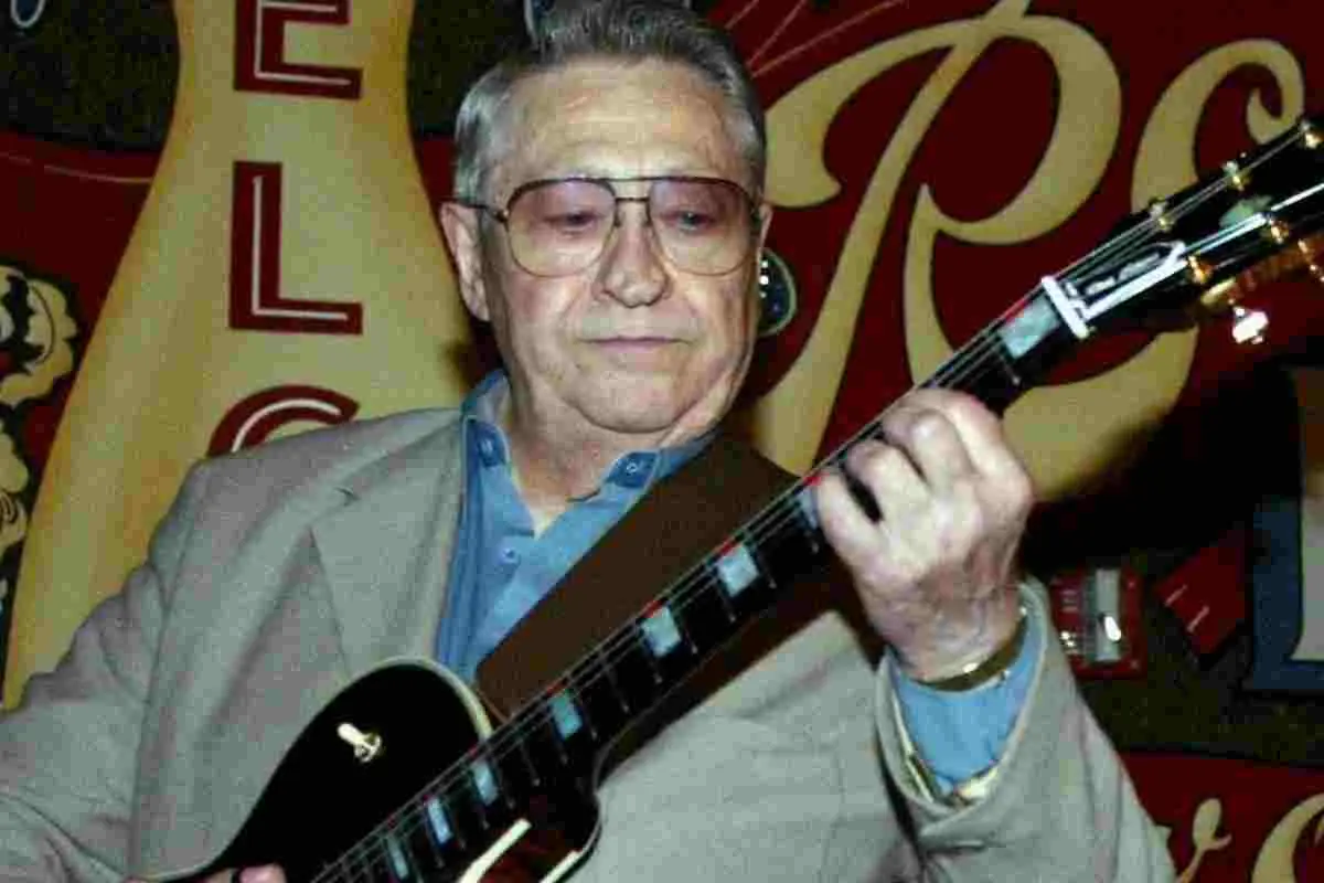 Scotty Moore playing electric guitar on stage, wearing glasses and a jacket.