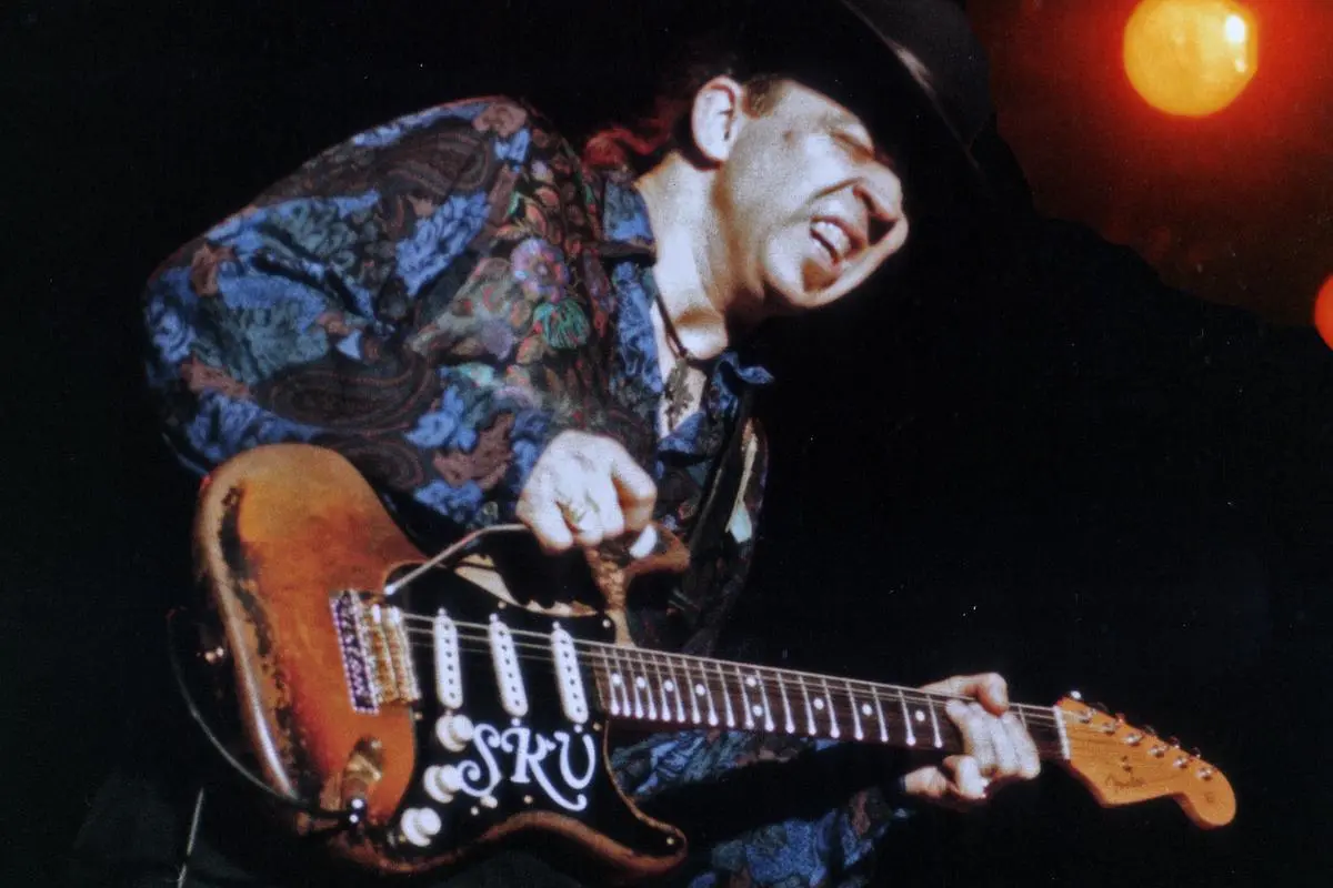 Stevie Ray Vaughan smiles mid-performance while playing his signature Stratocaster guitar.