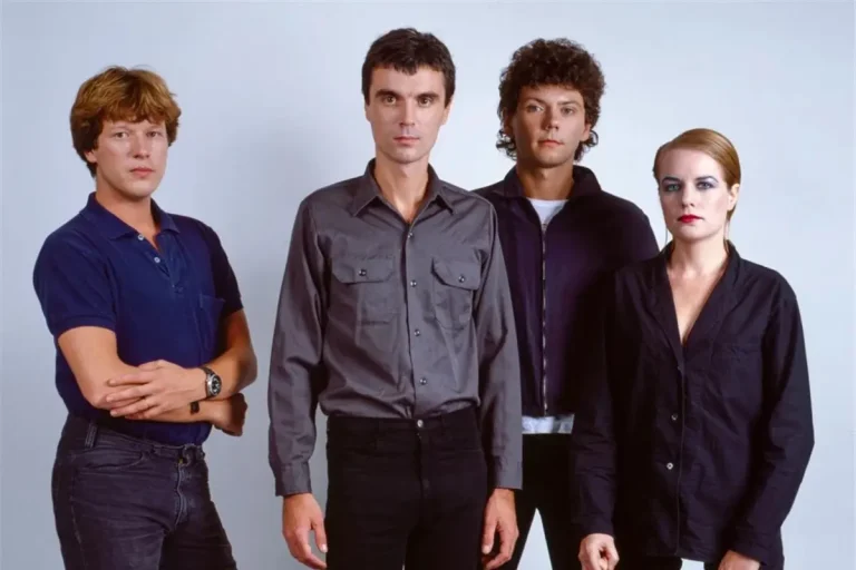Talking Heads band members stand side by side against a plain background, wearing minimalist late-1970s attire that reflects the band’s early art-rock aesthetic.