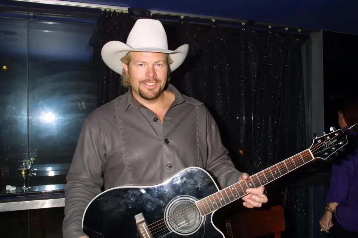 Toby Keith performing live on stage with an acoustic guitar, wearing a cowboy hat.