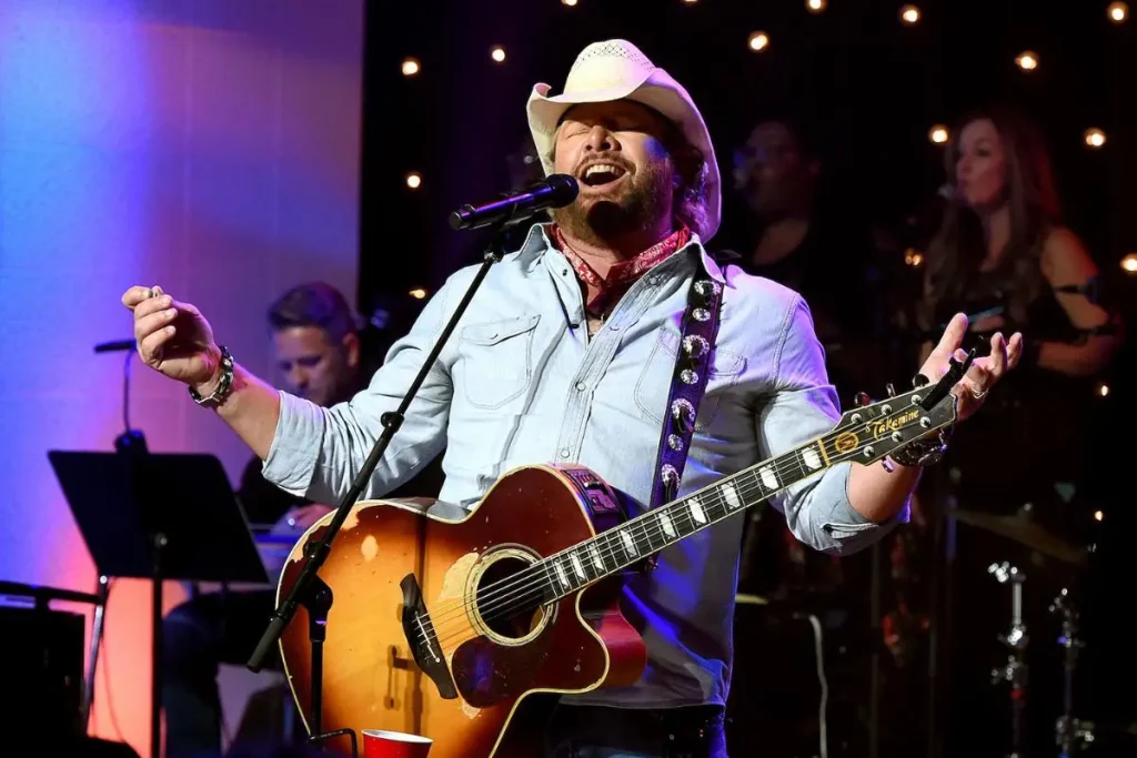 Toby Keith singing into a microphone during a live concert performance.