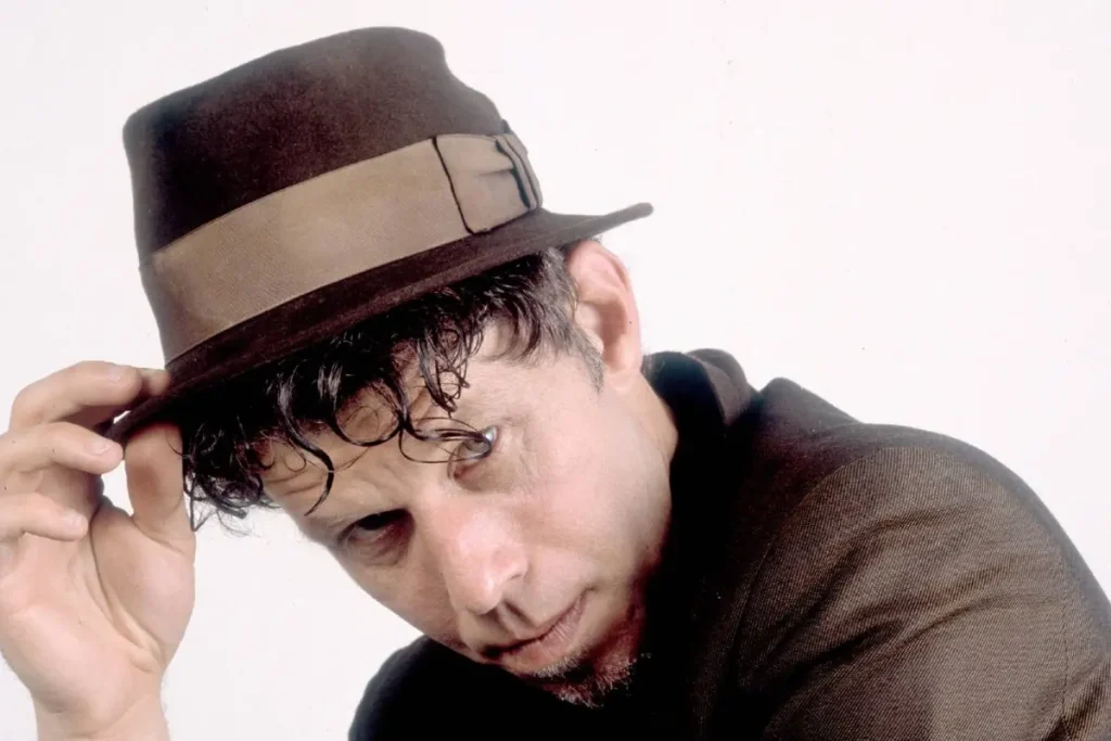 Tom Waits tilts his hat toward the camera in a stylized studio portrait, evoking his theatrical and blues-infused musical identity.
