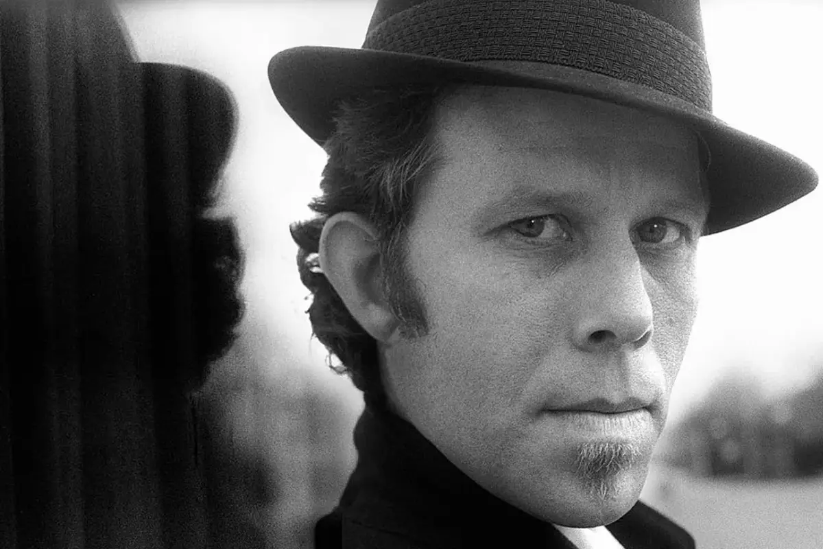 Close-up portrait of Tom Waits wearing a hat, his direct gaze and weathered expression reflecting his gritty, storytelling persona.