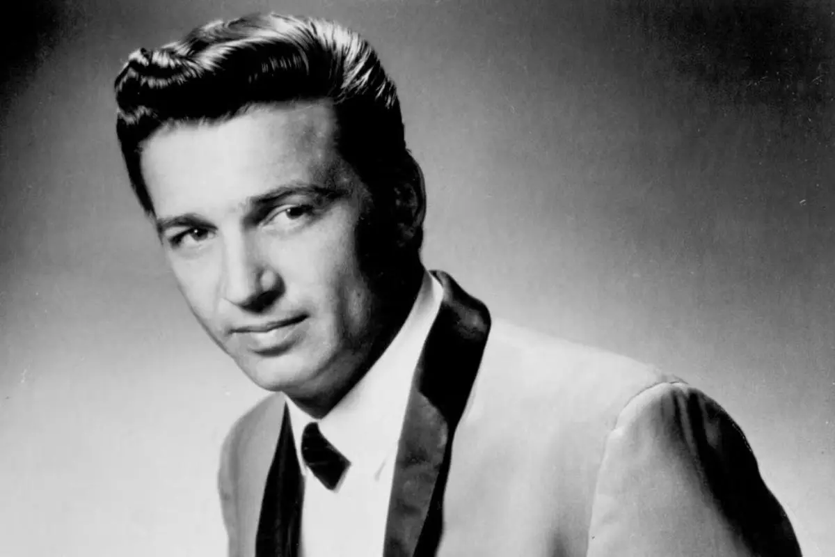 Waylon Jennings wearing a suit and bow tie, looking slightly to the side against a plain background.