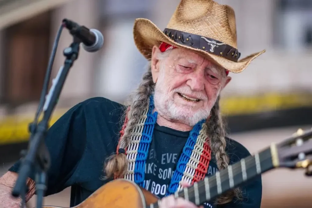 Willie Nelson performs on stage wearing a straw cowboy hat.