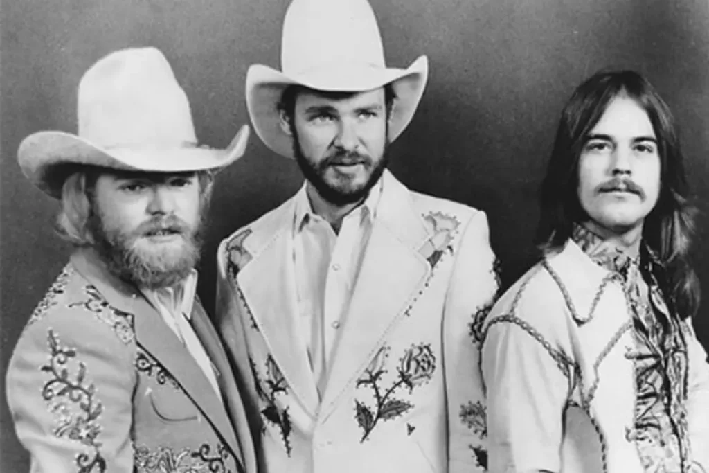 Early promotional portrait of the rock band ZZ Top wearing embroidered suits and cowboy hats, reflecting their Texas blues-rock image.