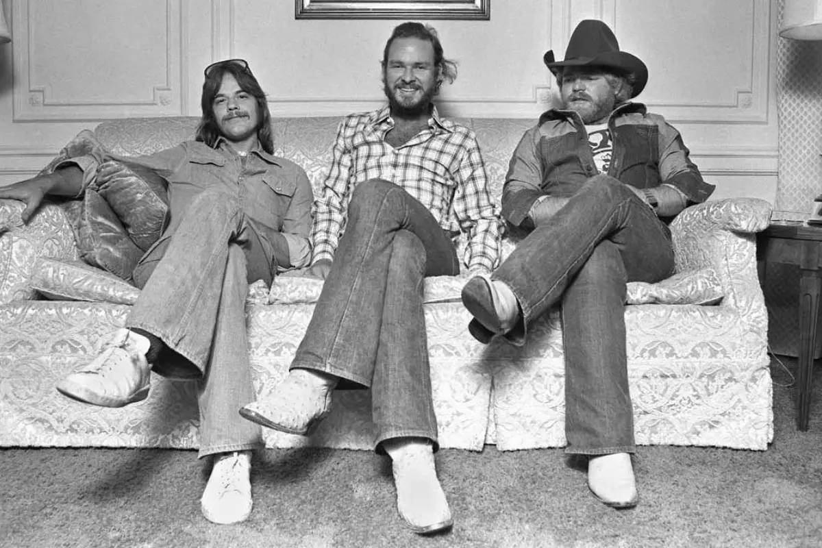 ZZ Top seated casually on a couch in a relaxed band photo, illustrating their grounded style and enduring chemistry as a trio.