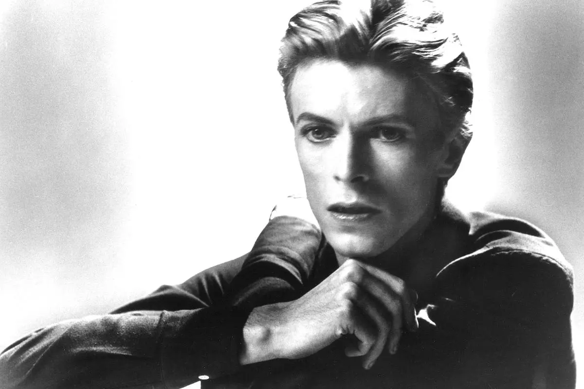 David Bowie in a black-and-white portrait, resting his chin on his hand with an intense, thoughtful expression.