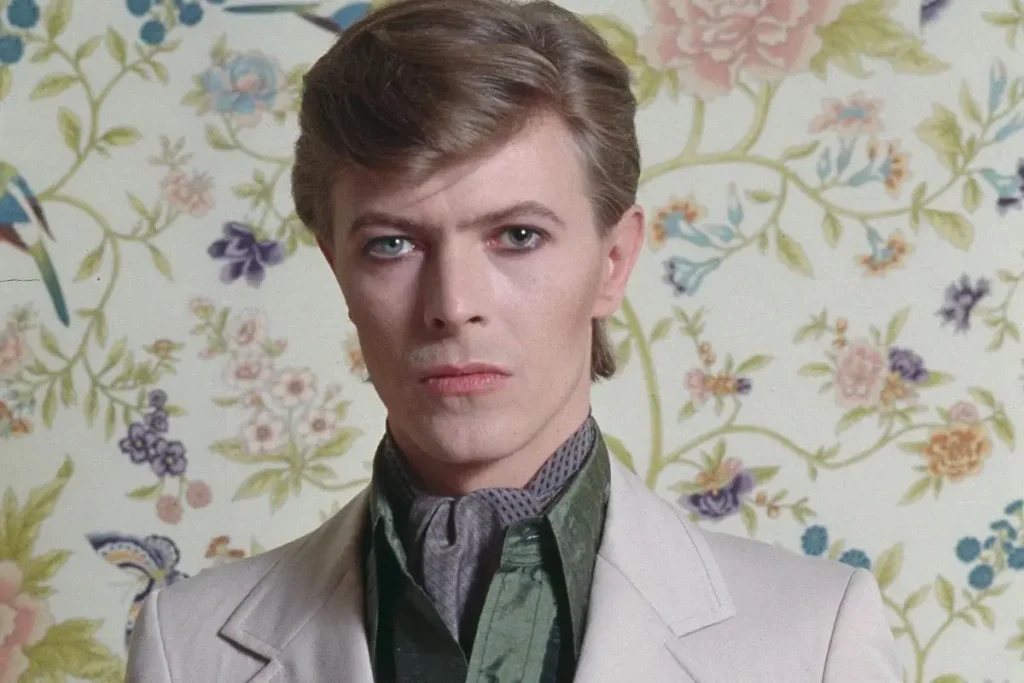 David Bowie in a color portrait wearing a light-colored suit and scarf.