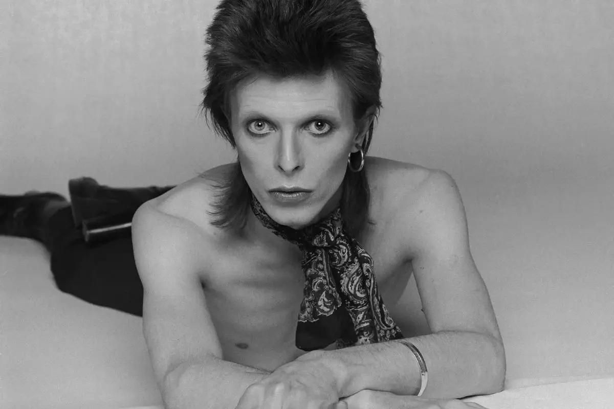 David Bowie in a black-and-white studio photo, shirtless and lying forward.