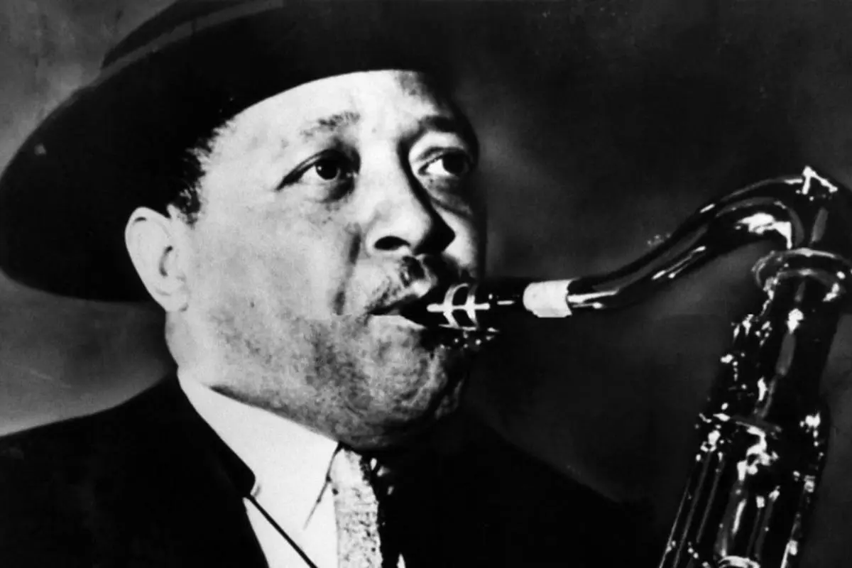lester young smiling and posing with an upright bass and an saxophone resting in front of him.