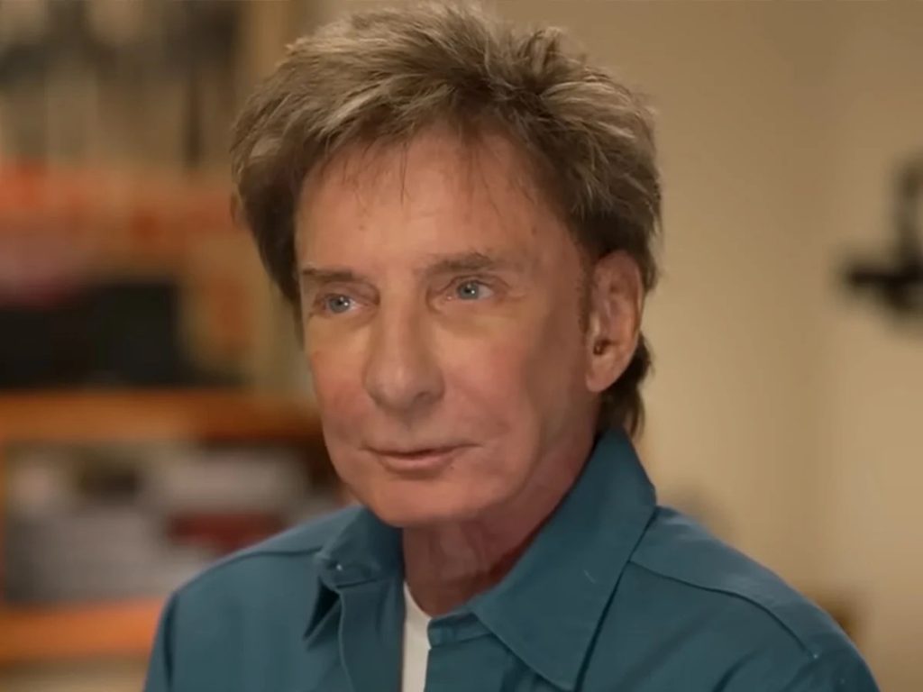 Barry Manilow speaking during a television interview, wearing a teal shirt
